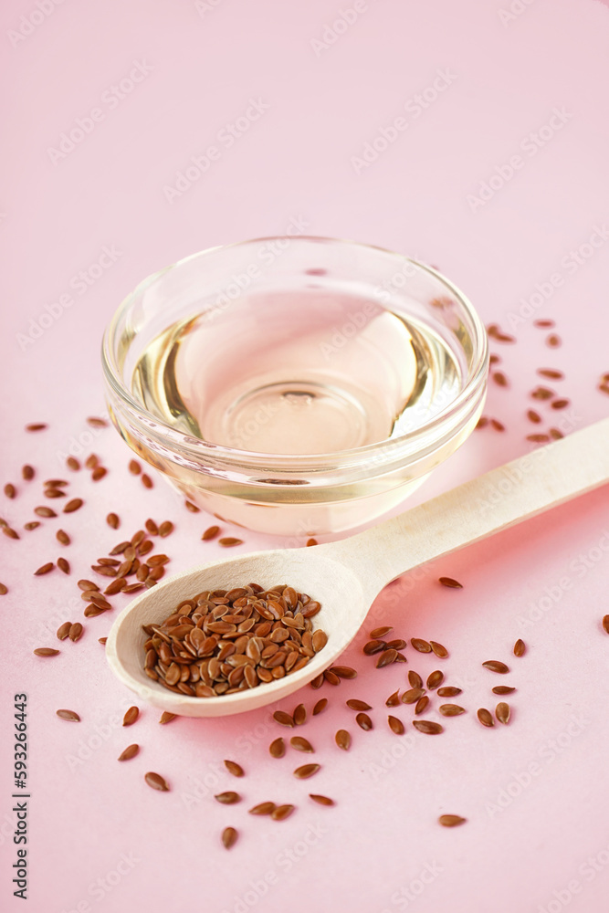 Bowl with flax oil and spoon of seeds on pink background