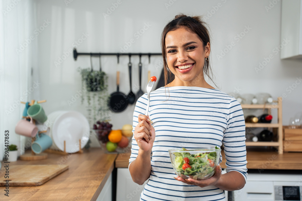 Portrait of young Caucasian girl eating green salad in kitchen at home. 