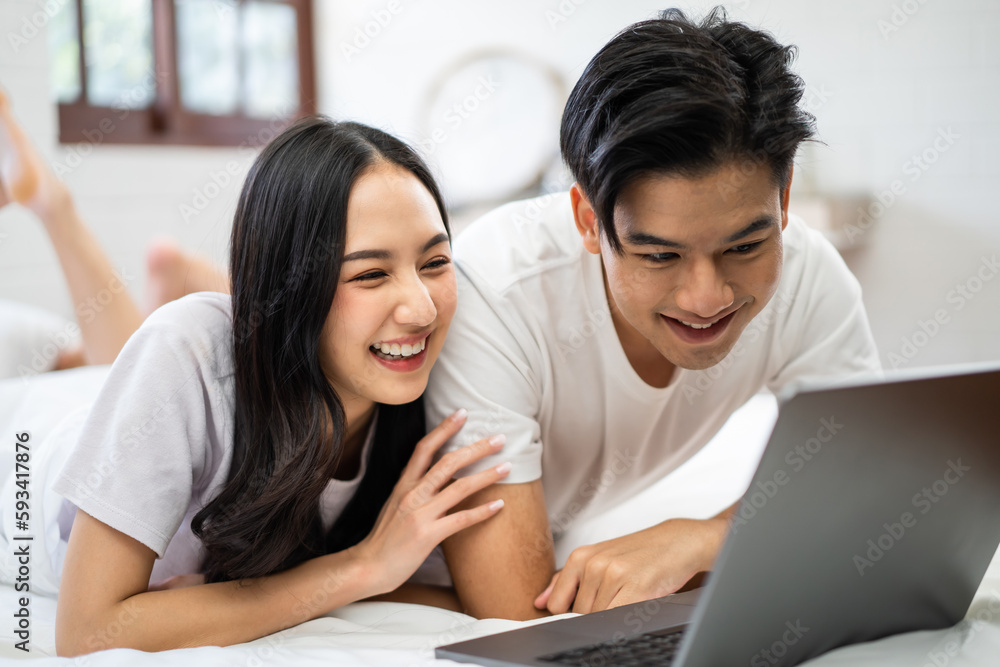 Asian attractive woman using laptop on bed with husband in the morning. 