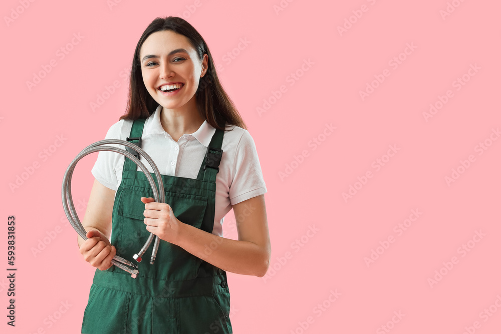 Female plumber with flexible hose on pink background