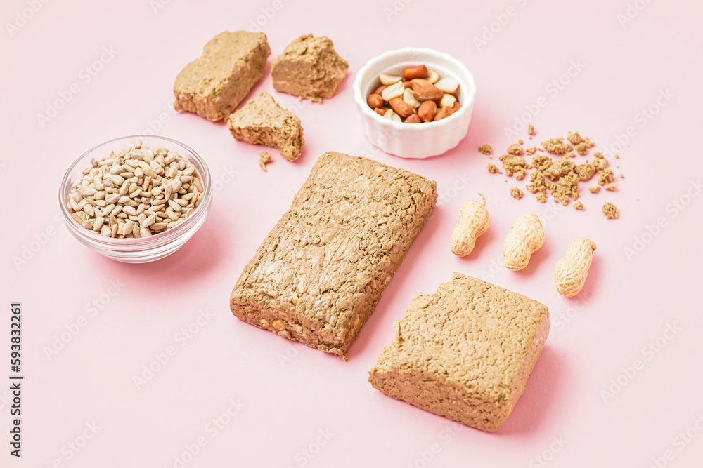 Composition with tasty halva, peanuts and sunflower seeds on pink background