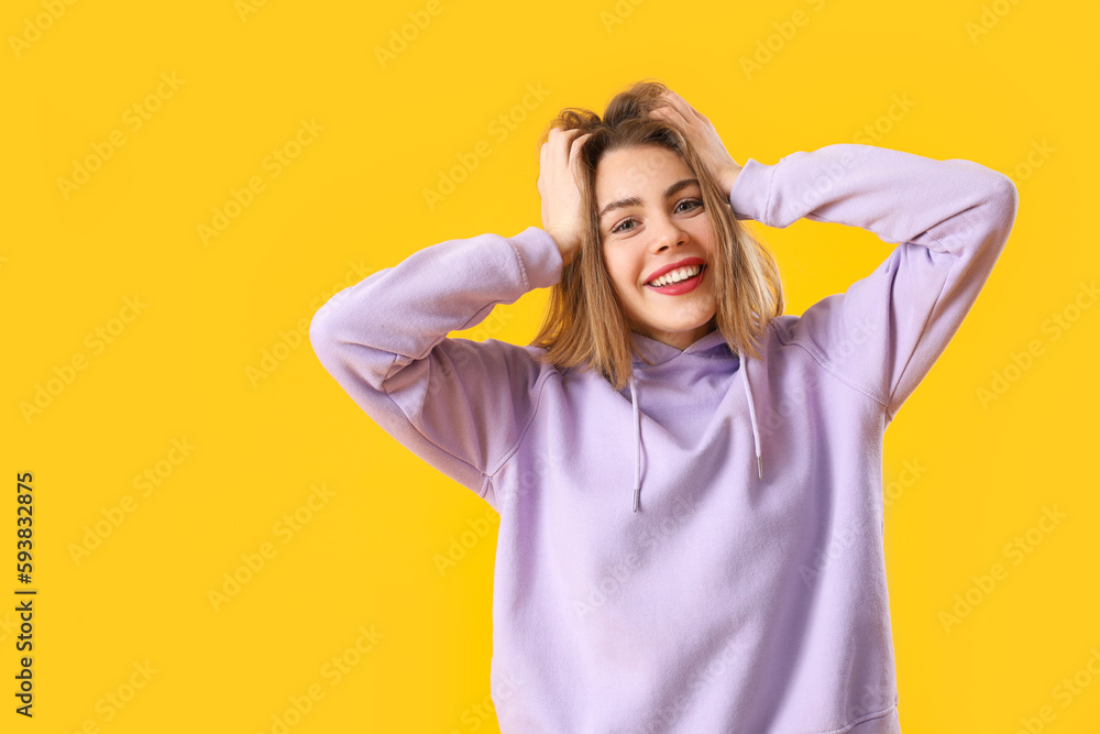 Happy young woman in lilac hoodie on yellow background