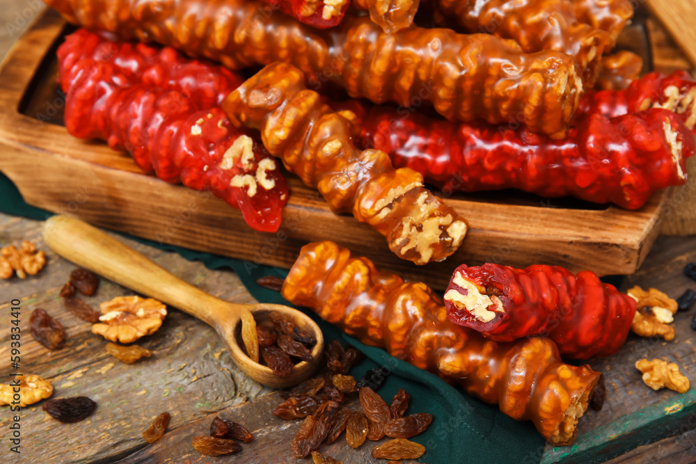 Board with delicious churchkhela and spoon of raisins on wooden table, closeup