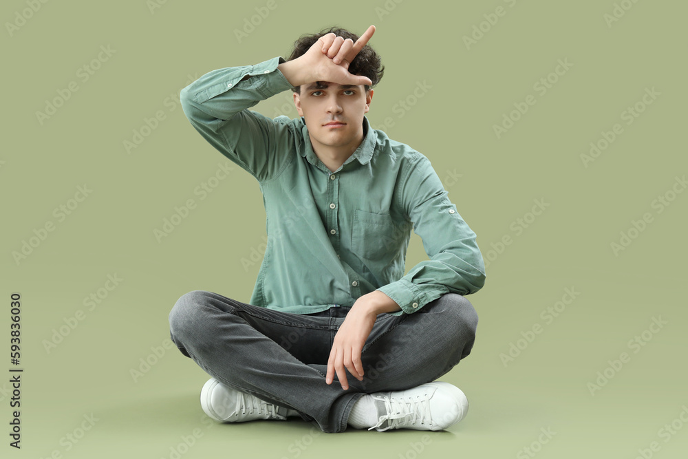 Young man showing loser gesture on green background