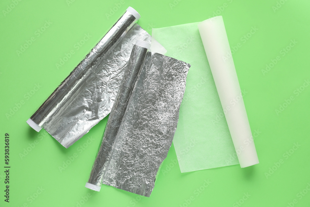 Rolls of baking paper and aluminium foil on green background