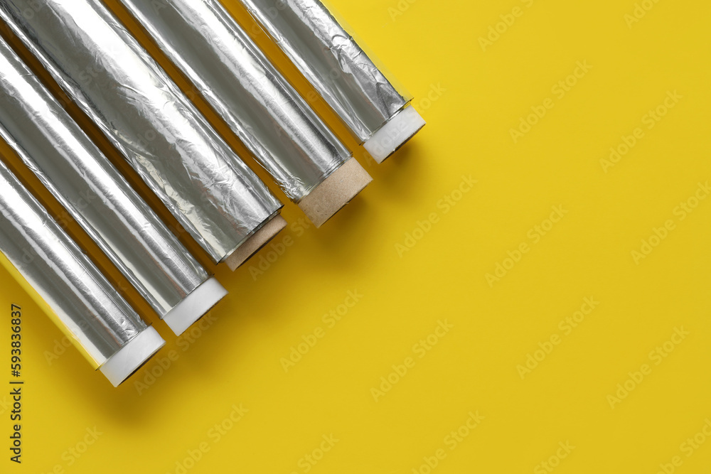 Aluminium foil rolls on yellow background, closeup