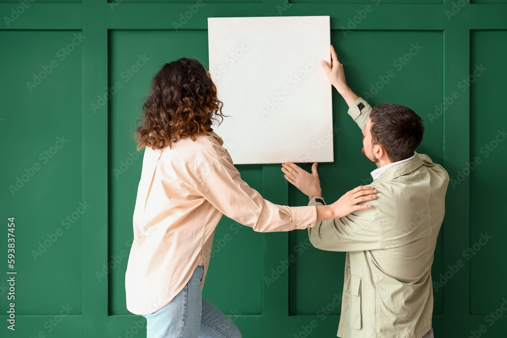 Young couple hanging blank poster on green wall at home