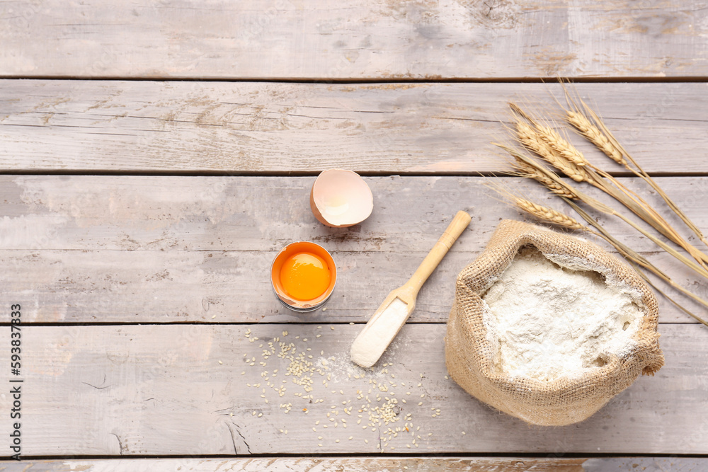 Composition with sack bag of wheat flour and cracked egg on grey wooden table