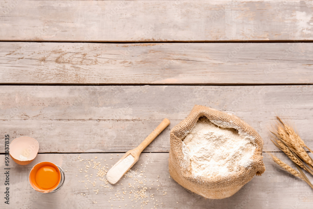 Composition with sack bag of wheat flour and cracked egg on grey wooden table