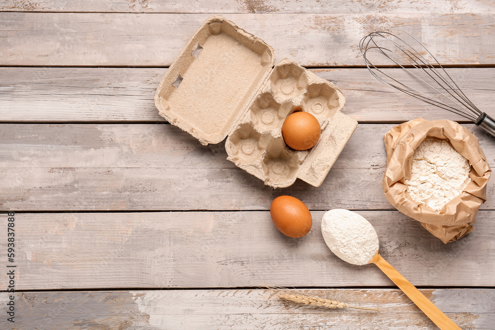 Composition with paper bag of wheat flour, spoon and eggs on grey wooden table