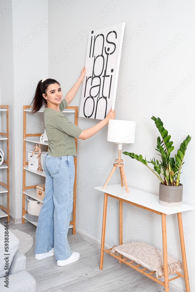 Young woman hanging picture on wall in living room