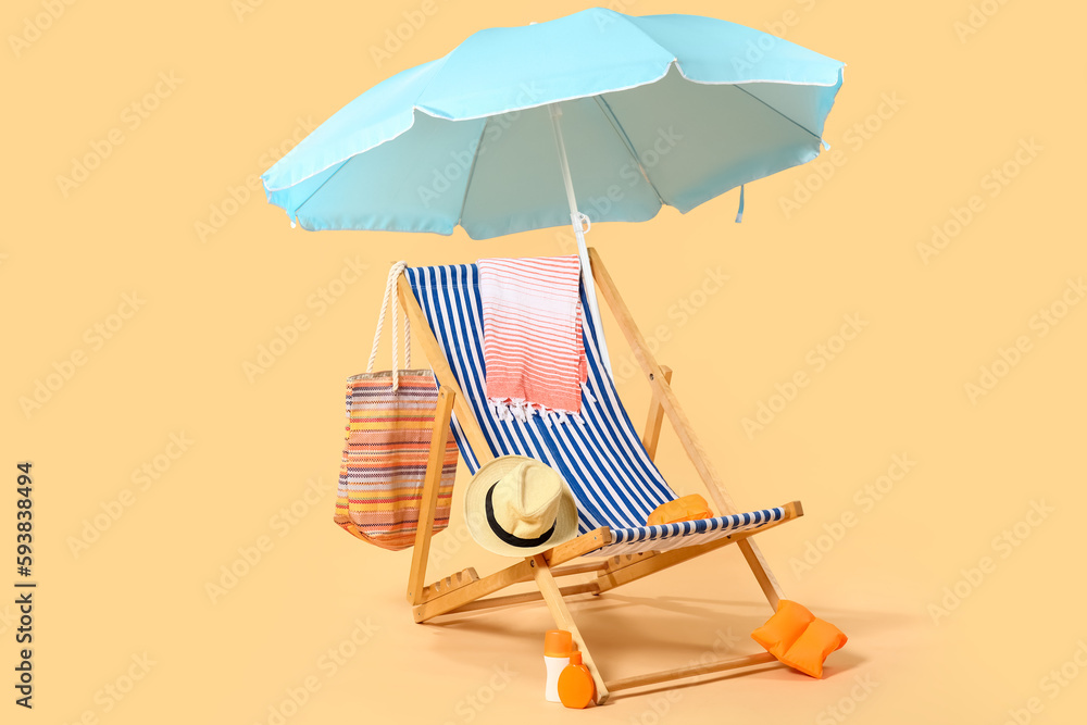 Deck chair, blue umbrella and beach accessories on beige background