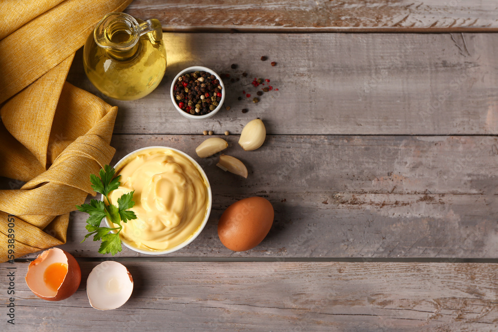 Bowl with tasty mayonnaise sauce and ingredients on grey wooden background