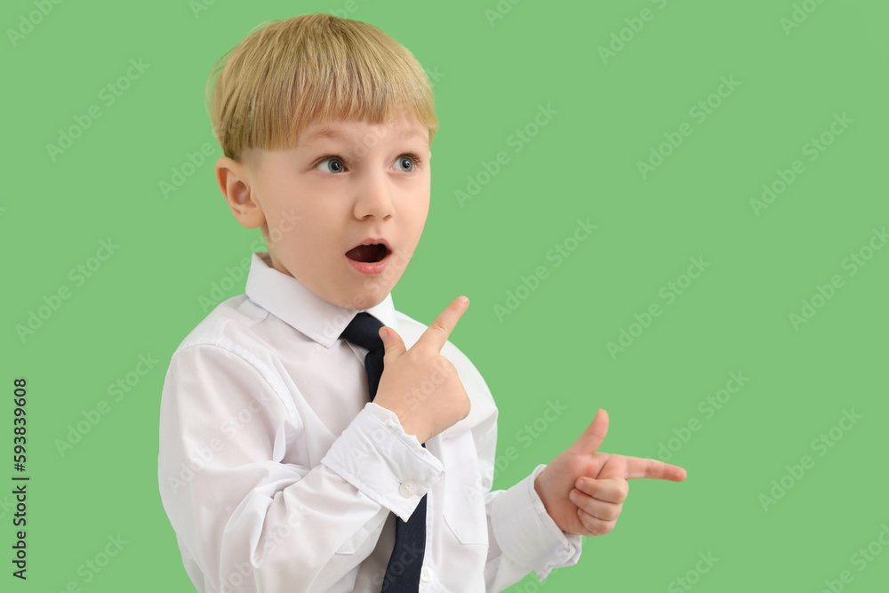 Shocked little businessman pointing at something on green background