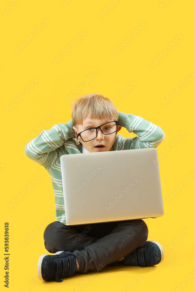 Shocked little businessman with laptop sitting on yellow background