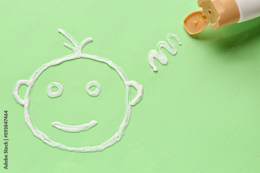 Drawing of baby face made with sunscreen cream on green background