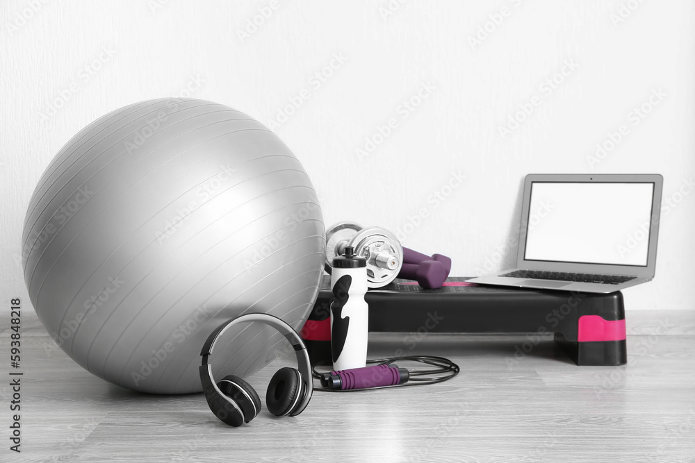 Laptop with sports equipment and headphones near white wall in gym