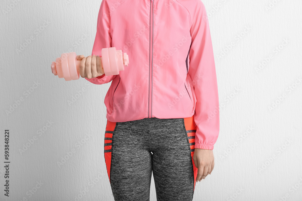 Sporty woman with dumbbell near white wall