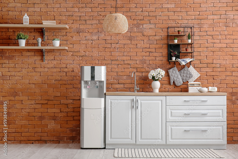 Interior of kitchen with modern water cooler near brick wall