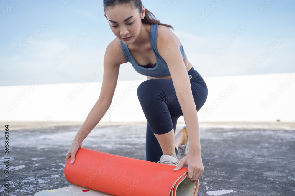 Young Asian woman picking up yoga mat after exercising.outdoor exercise fitness concept