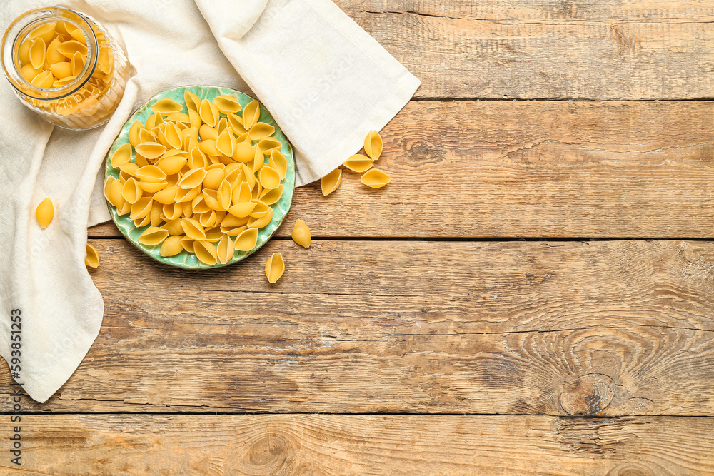 Plate and jar with raw conchiglie pasta on wooden background