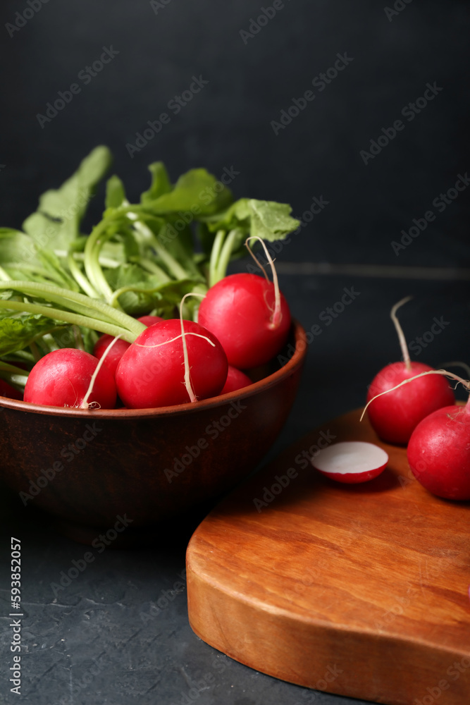 Bowl of ripe radish with green leaves on dark background, closeup