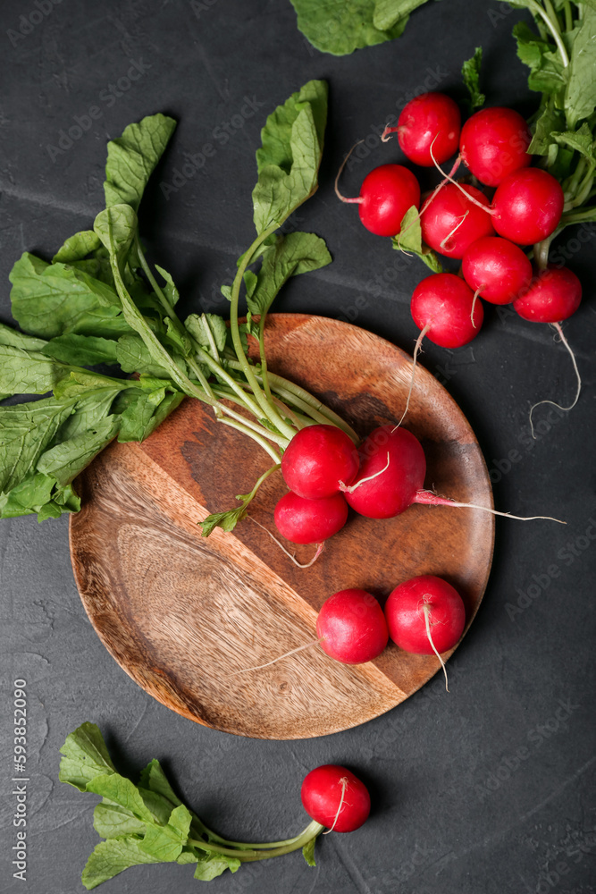 Plate of ripe radish with green leaves on dark background