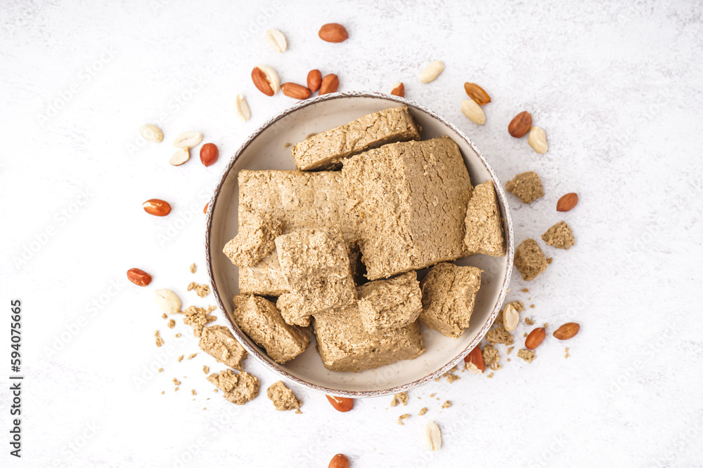 Bowl with pieces of tasty halva and peanuts on light background