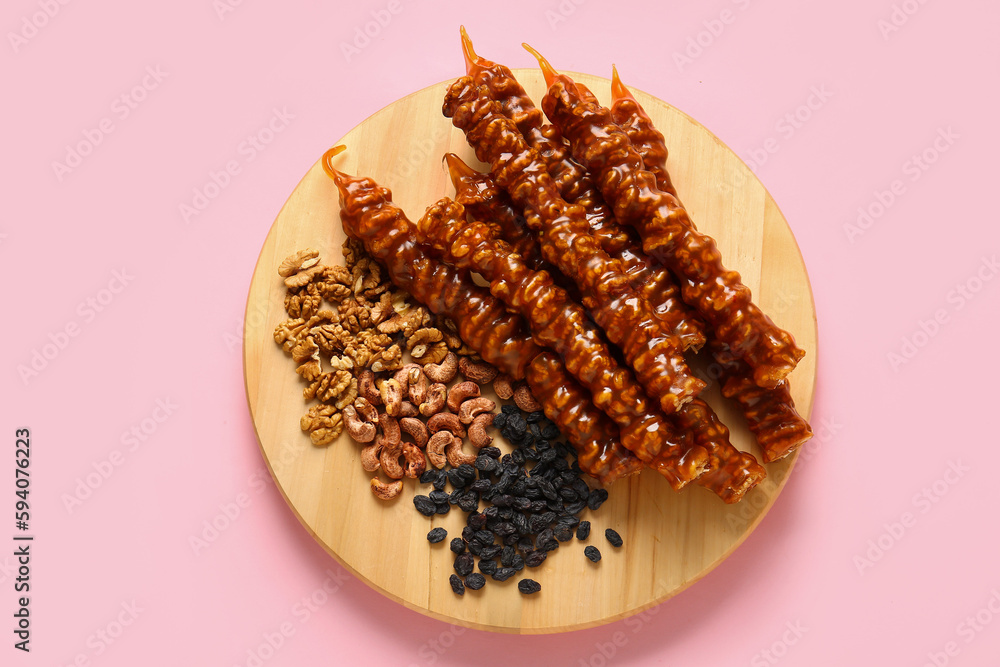 Wooden board with tasty churchkhela, raisin and nuts on pink background