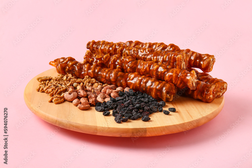 Wooden board with tasty churchkhela, raisin and nuts on pink background