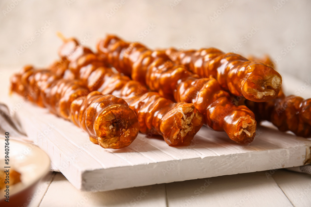 Board with tasty churchkhela on light wooden table, closeup