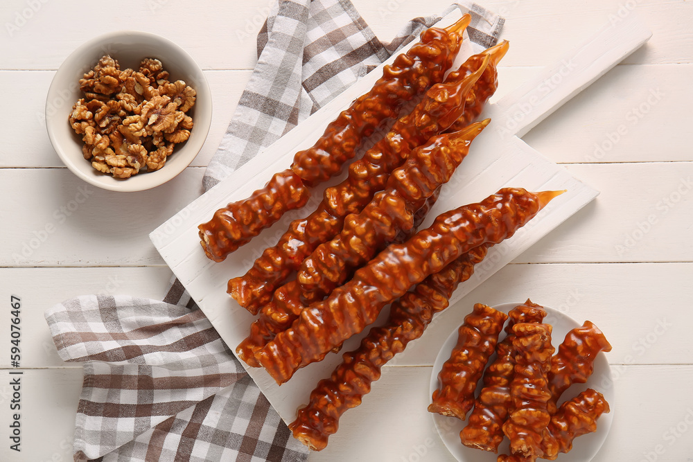 Board with tasty churchkhela and walnuts on light wooden background