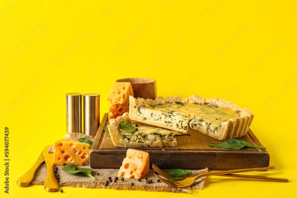 Board with pieces of delicious quiche and cheese on yellow background