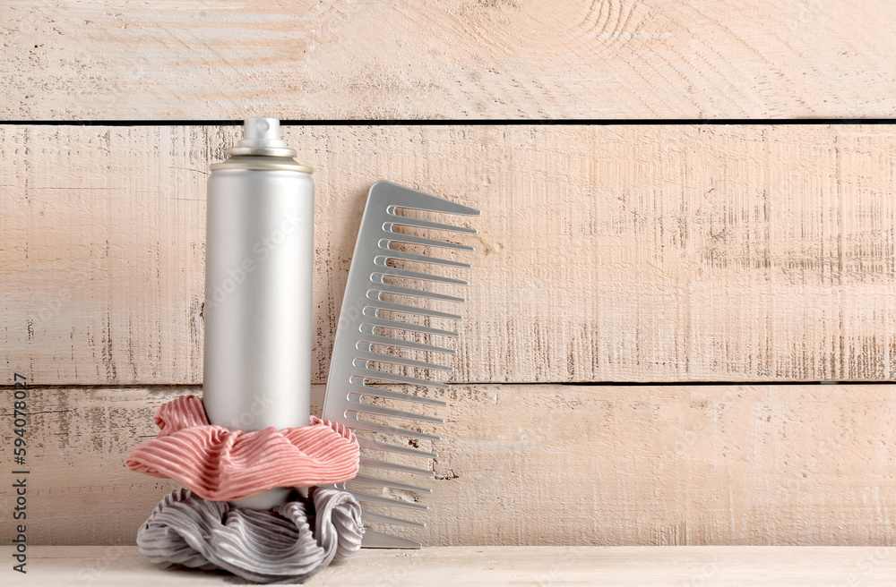 Bottle of hair spray, scrunchy and brush on light wooden background