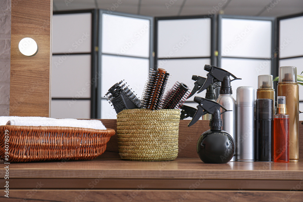 Different hair sprays and brushes on table in beauty salon