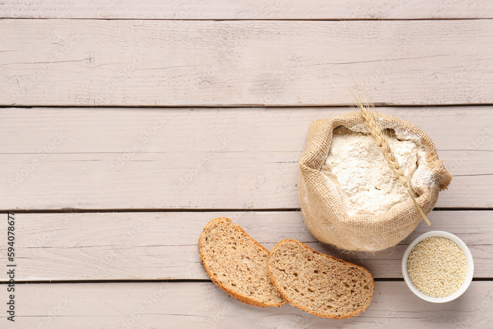 Sack bag of wheat flour, sesame seeds and pieces of bread on grey wooden table