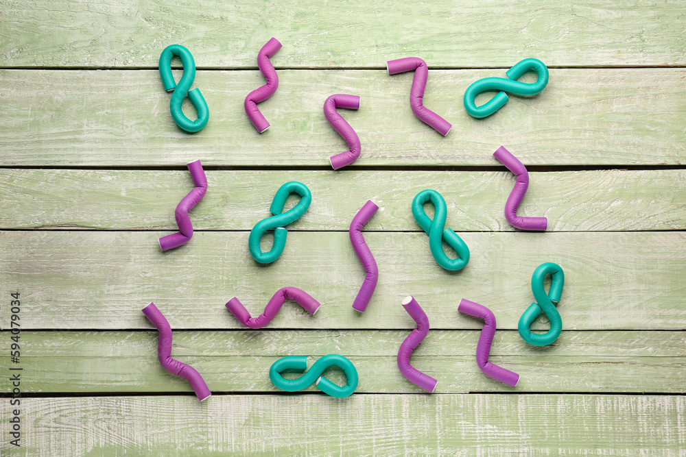 Hair curlers on green wooden background