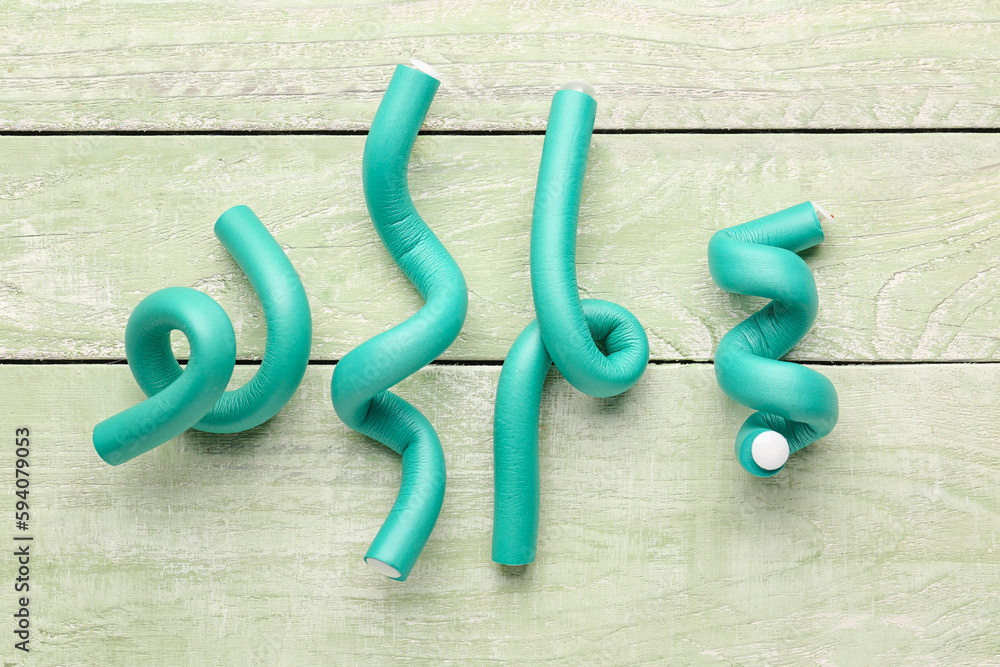 Hair curlers on green wooden background