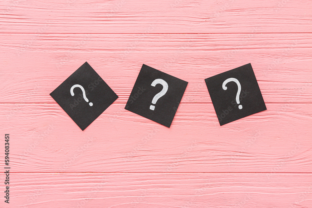 Papers with question marks on pink wooden background