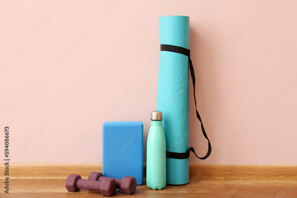 Dumbbells with fitness mat, block and bottle near pink wall