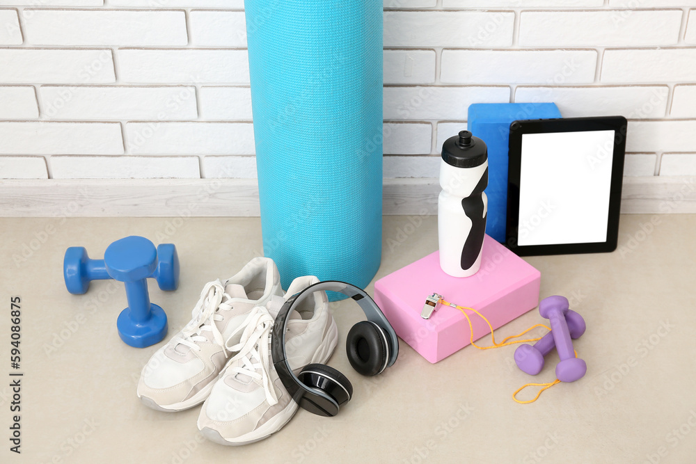 Sports equipment with headphones, tablet computer and bottle near white brick wall