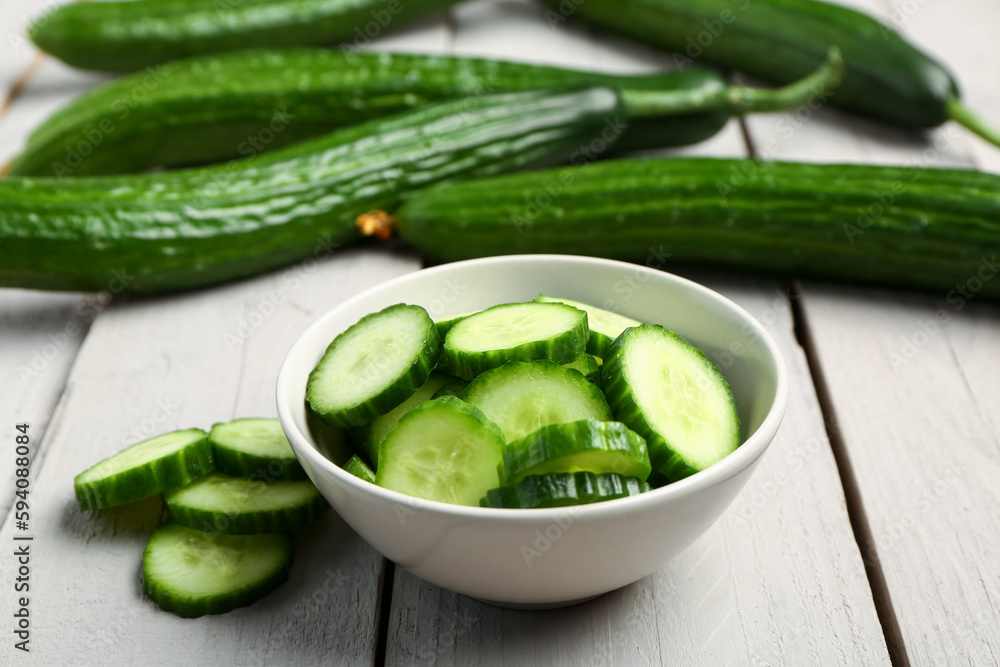 Bowl with fresh cut cucumber on light wooden background