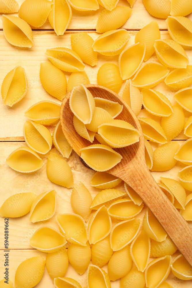 Heap of raw conchiglie pasta and spoon on wooden background