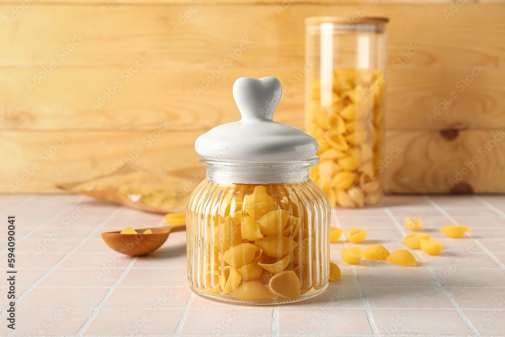 Jar with raw conchiglie pasta on table