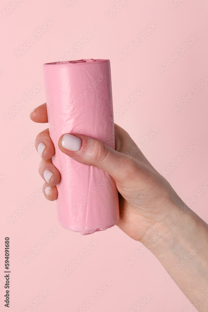 Female hand holding roll of garbage bags on pink background