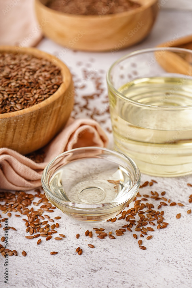 Glass and bowl with flax oil and seeds on light background