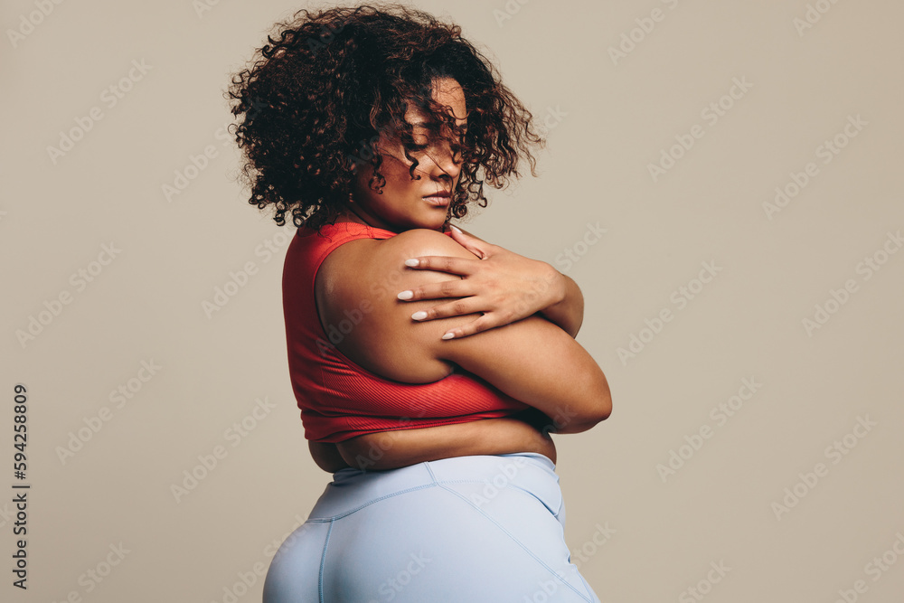 Confident woman embracing her body in a studio, wearing a sportswear outfit