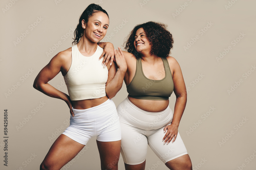 Athletic and proud, two female friends stand in gym wear showing their fit bodies