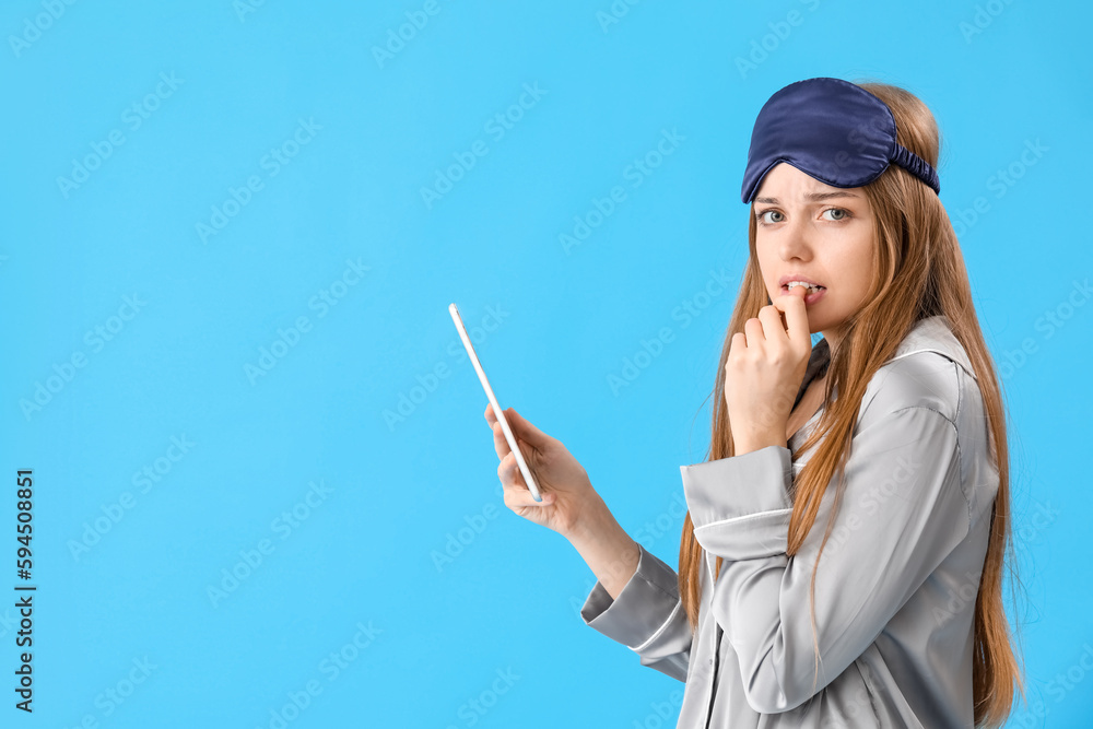 Young woman with tablet computer biting nails on blue background