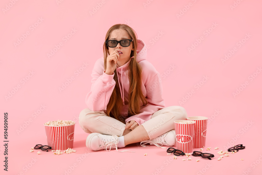 Young woman in 3D glasses with popcorn biting nails on pink background